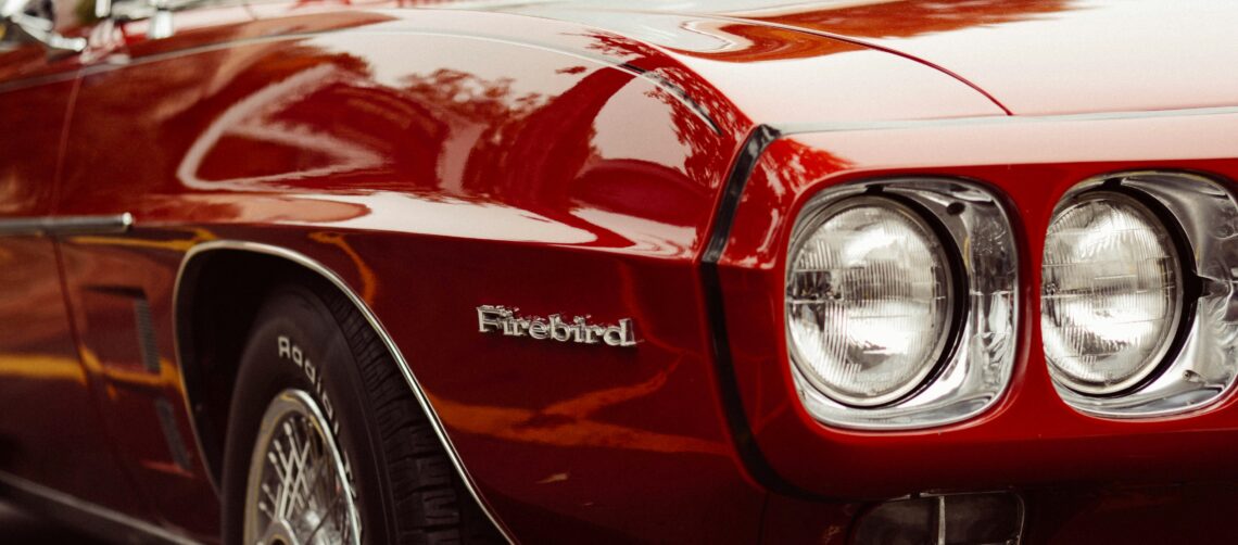 Photo of a dark red old Firebird car with black pinstripes. Photo by David Straight on Unsplash