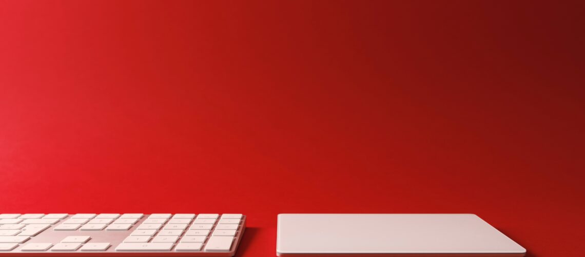 A photo of a computer keyboard and trackpad against a gradient red background.