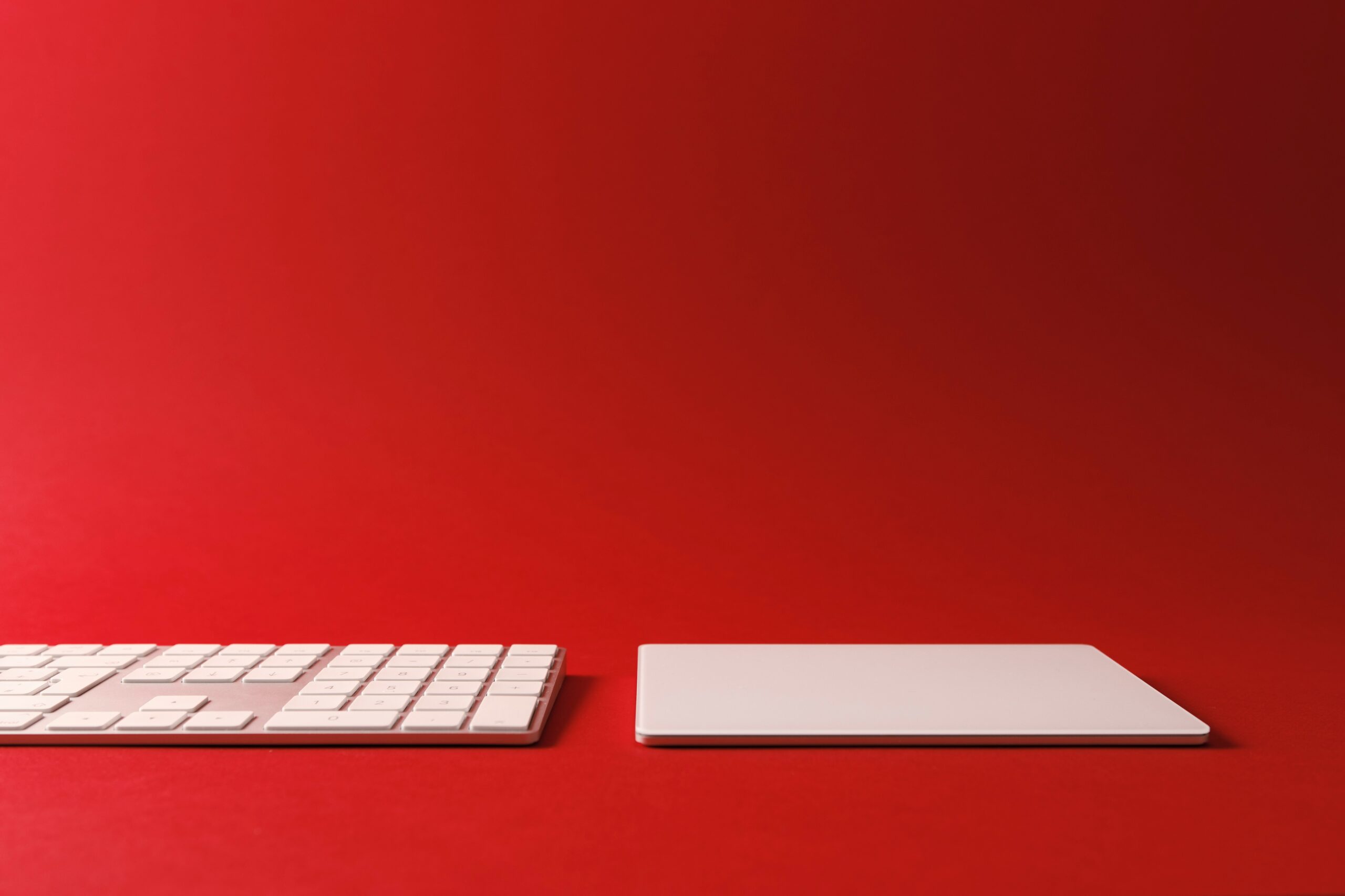 A photo of a computer keyboard and trackpad against a gradient red background.